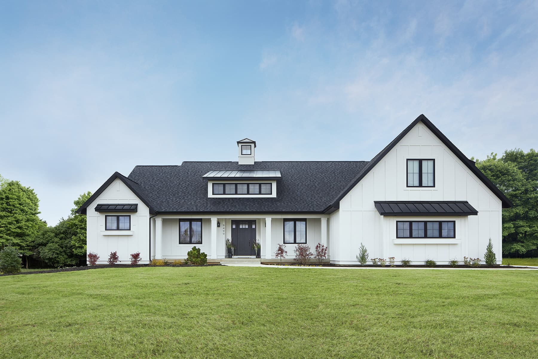 A white modern-farmhouse ranch clad in cellular-PVC board-and-batten siding with black-framed windows and a black metal roof