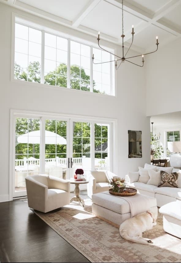 A bright two-story great room with white grid windows and white French doors opening to a covered porch