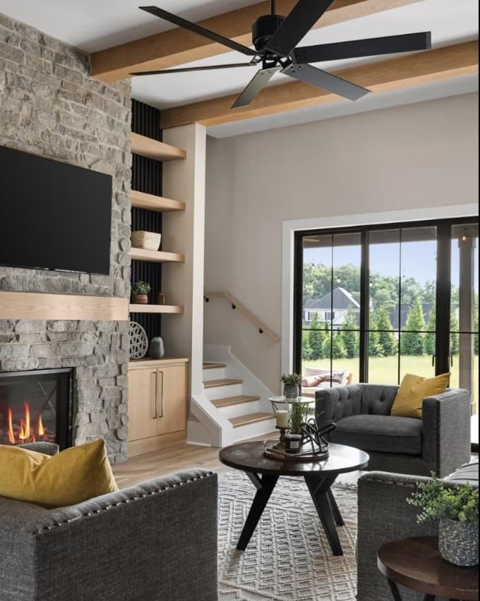 A living room with a stone fireplace and wood-beam ceiling, with black-framed sliding glass doors opening to the backyard