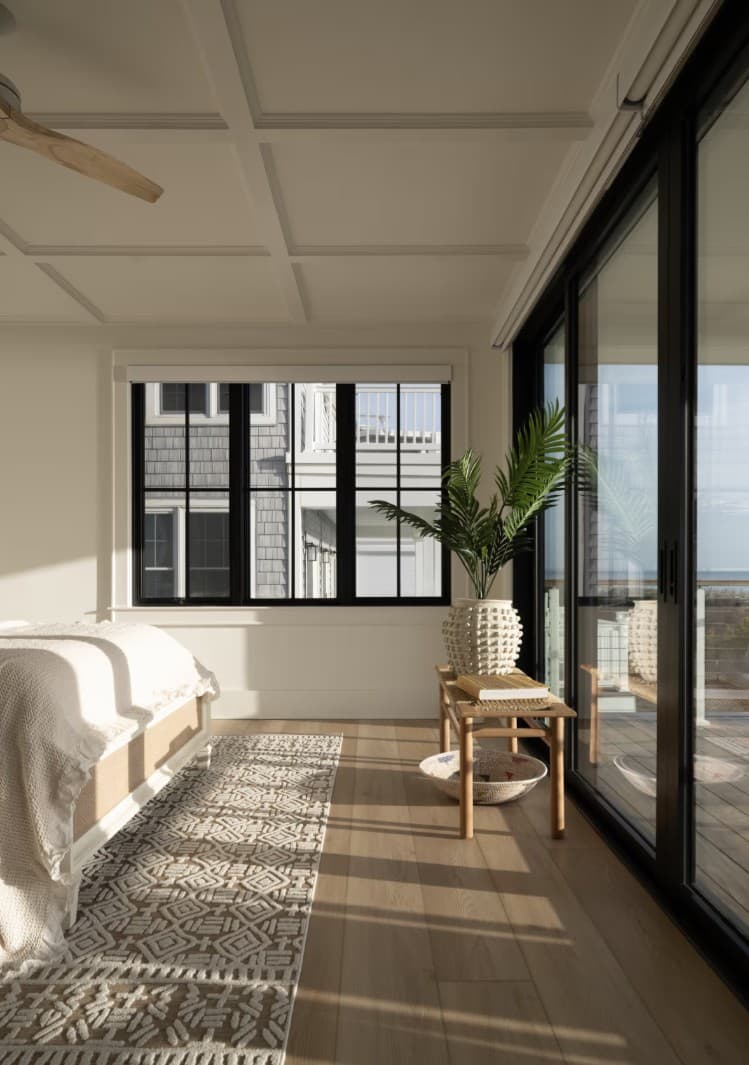 A coastal bedroom with black-framed windows and black sliding glass doors opening to a balcony with an ocean view