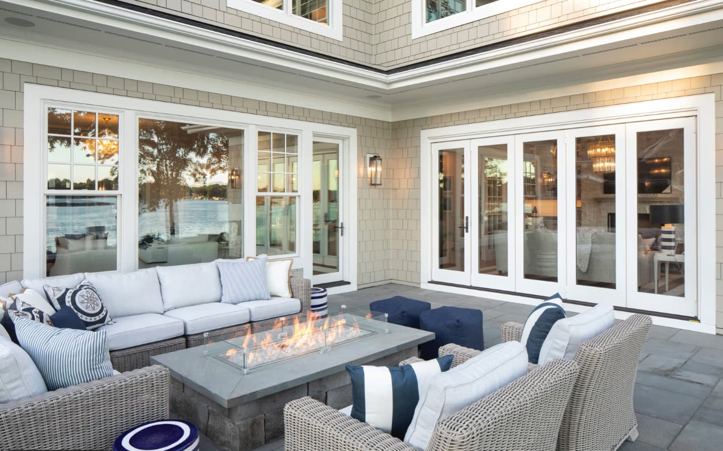 A coastal courtyard patio with white grid windows and folding glass doors on a shingle home overlooking the water