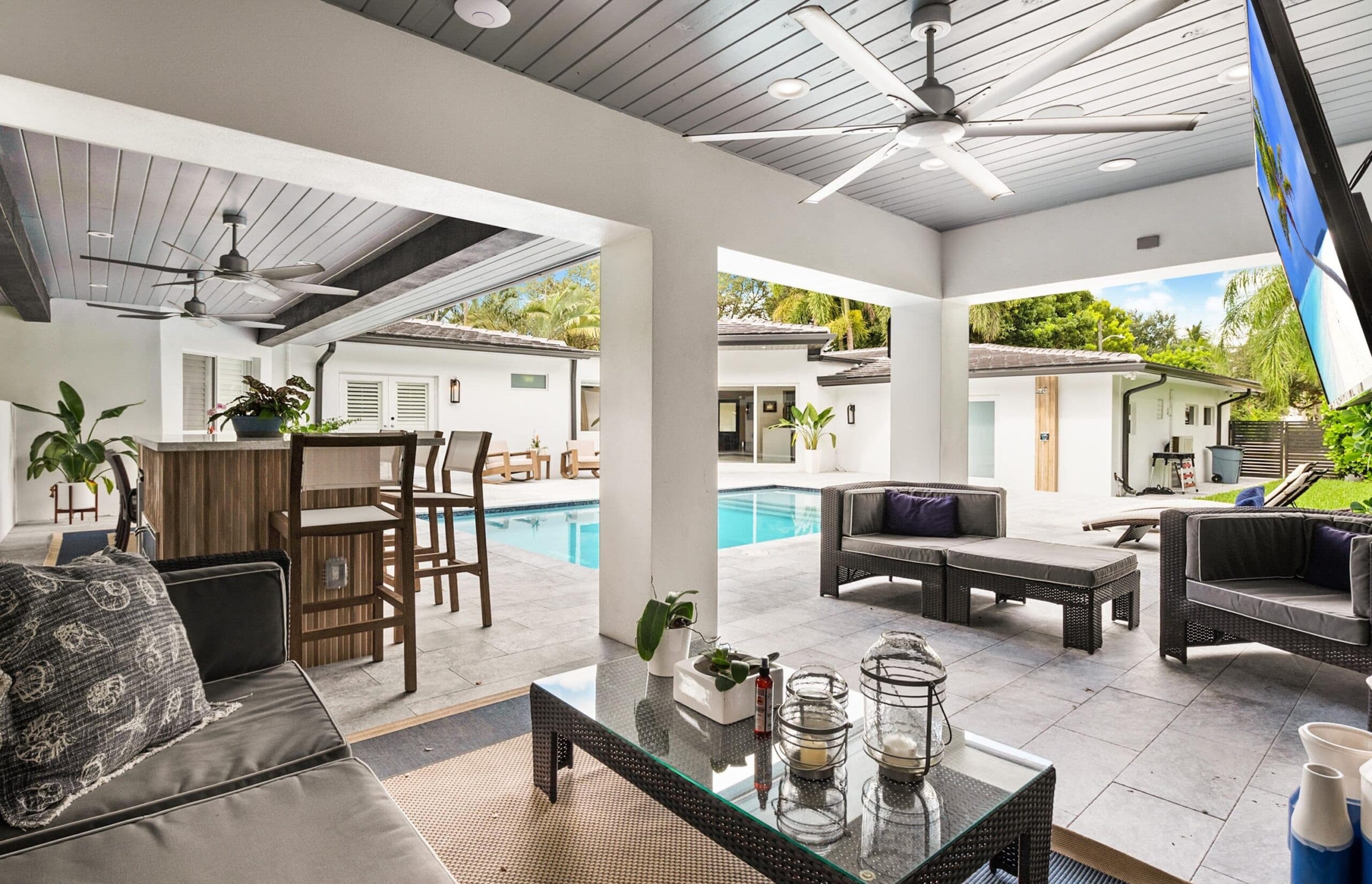 A covered poolside lanai with a wood-plank ceiling that opens fully to the patio and pool