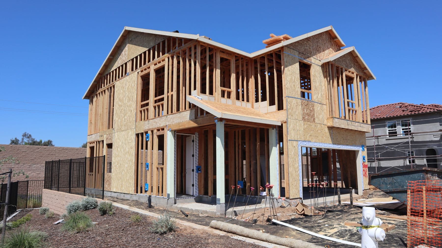 A two-story house under construction with full wood stud framing and sheathing