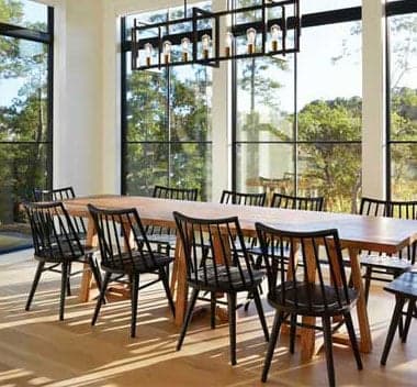A dining room wrapped in tall black-framed Andersen 400 Series windows overlooking woods
