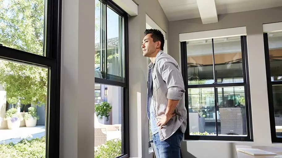 A person looking out through a tall black 100 Series single-hung Andersen window