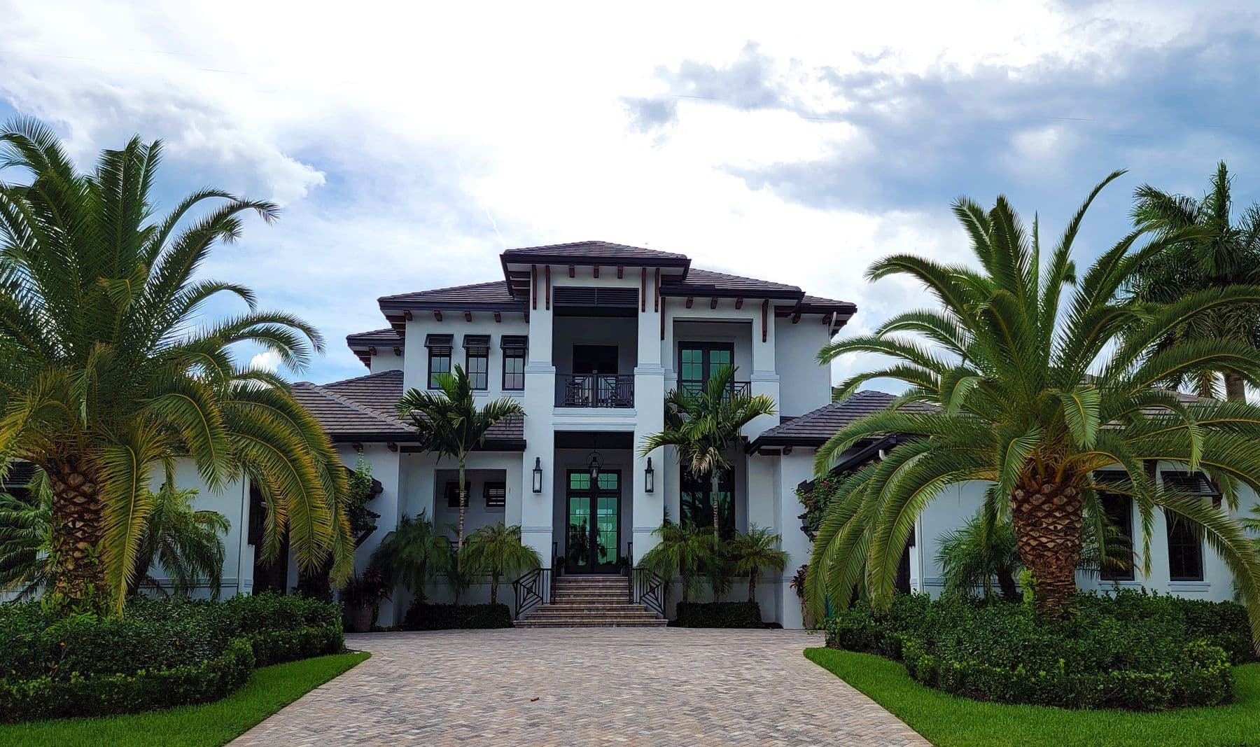 A large white coastal custom home framed by palm trees under a dramatic sky
