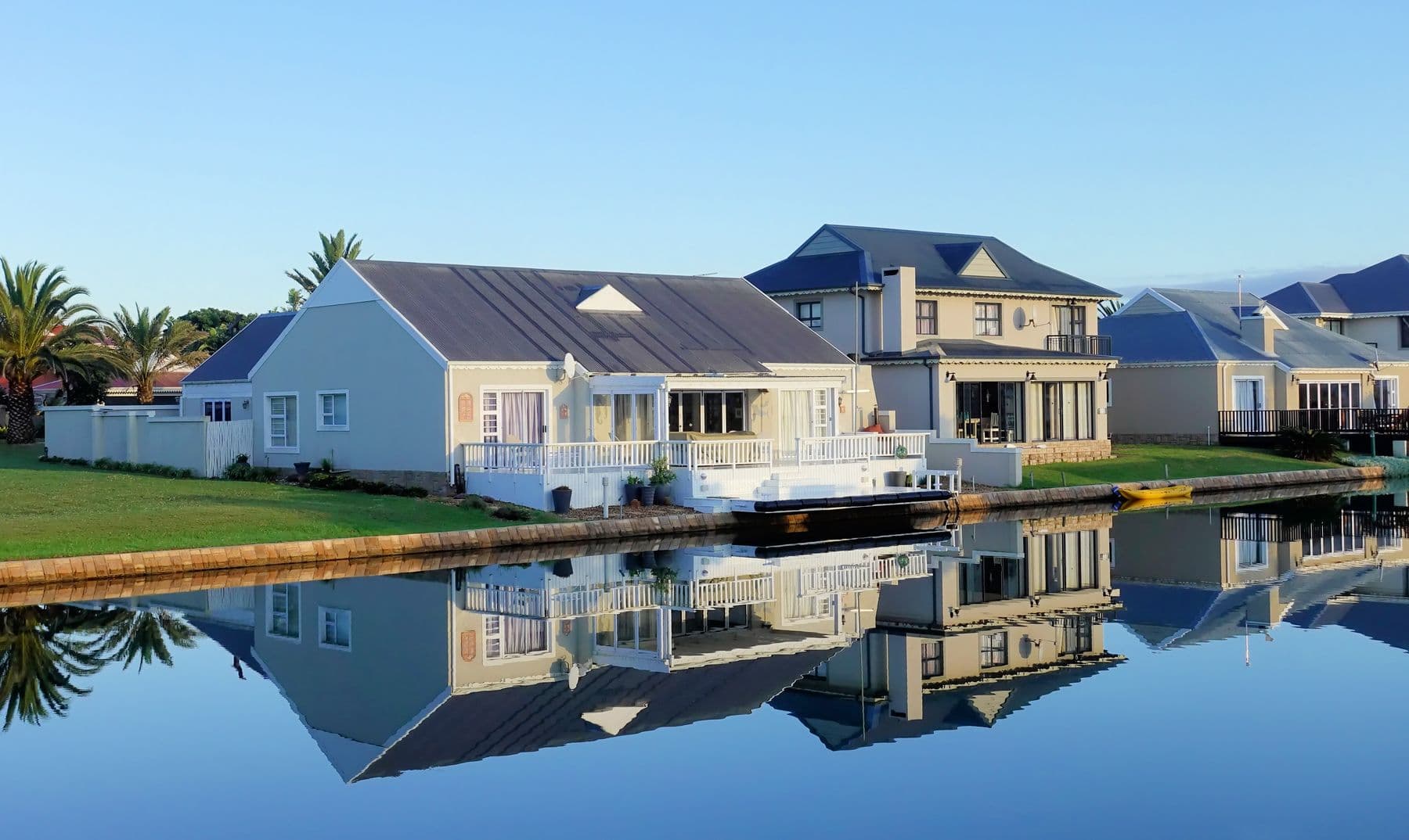 A row of white coastal homes with porches mirrored in a calm waterway