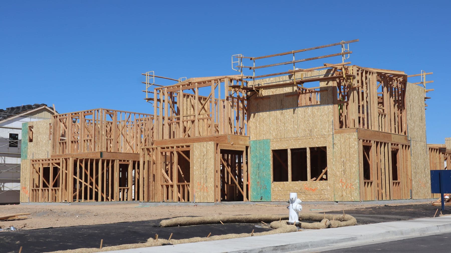 A two-story home under construction showing exposed wood stud framing against a blue sky